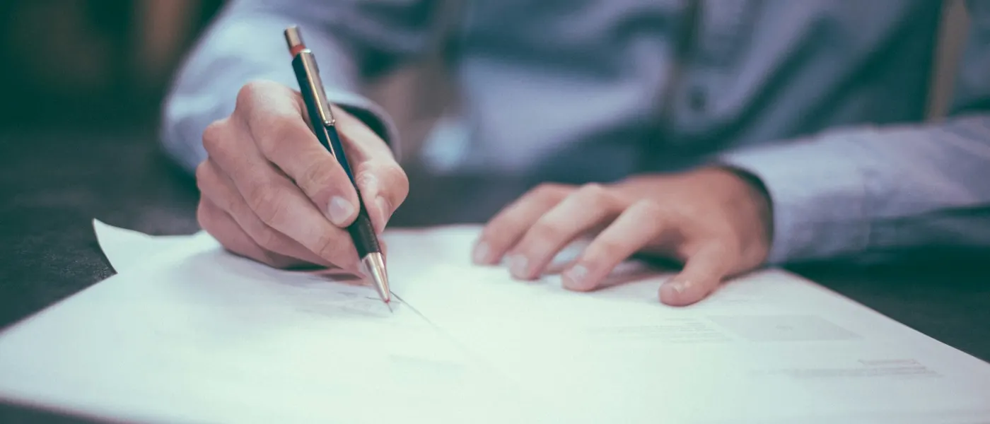Person signing a printed agreement with a pen